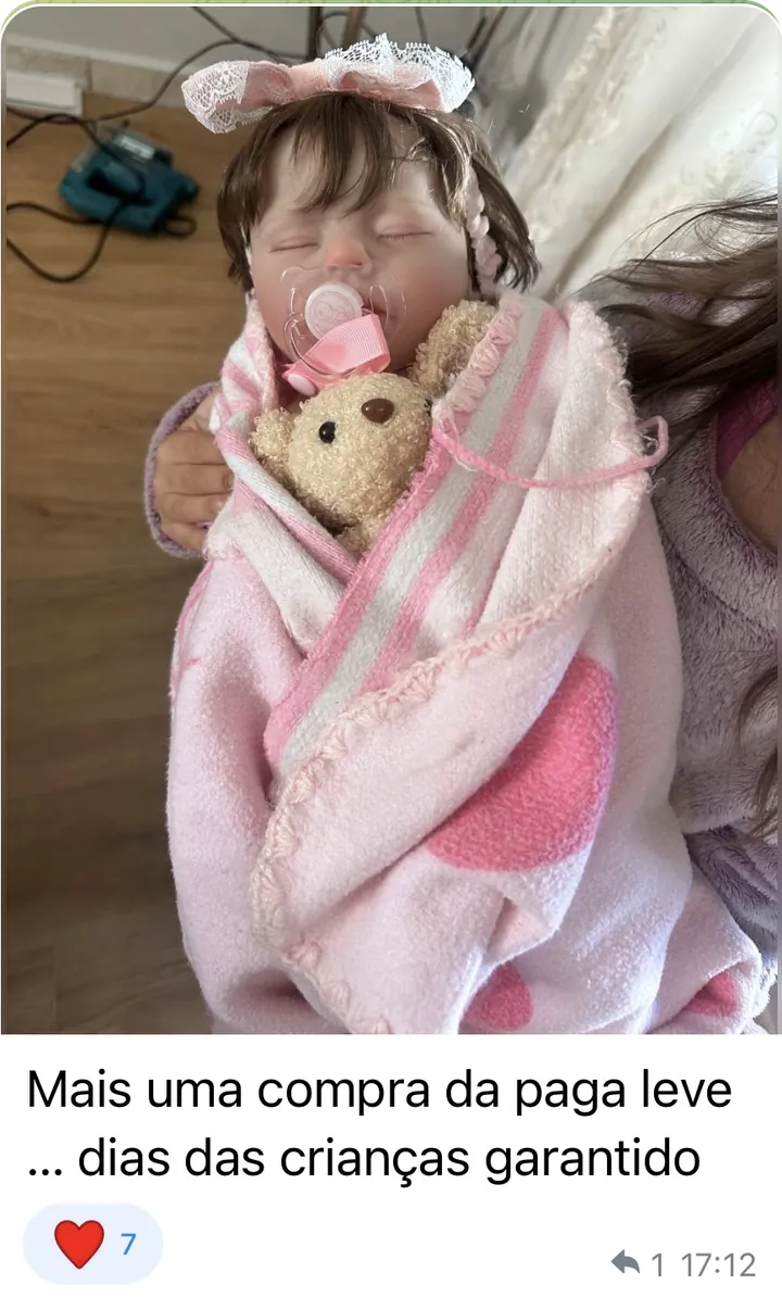 Foto de uma boneca bebê reborn embrulhada numa manta rosa, com a legenda “Mais uma compra da paga leve… dias das crianças garantido”